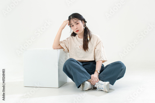 Portrait isolated cutout studio shot of Asian young cute female teenage fashion model with pigtails braids hairstyle in casual trendy wear sitting on floor posing look at camera on white background