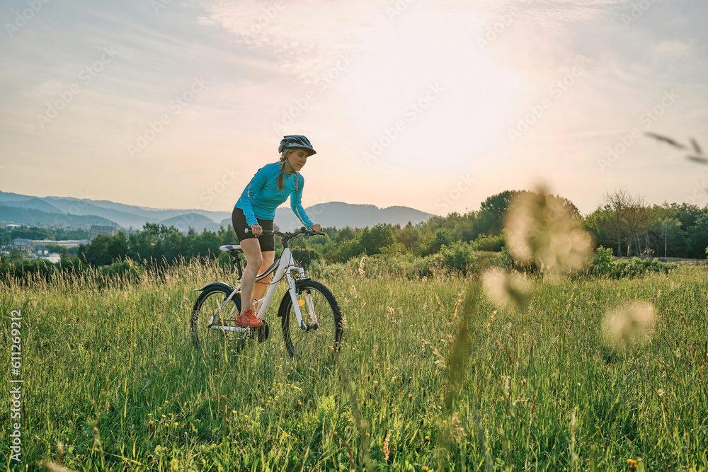 Obraz premium Cyclist Woman riding bike in helmets go in sports outdoors on sunny day a mountain in the forest. Silhouette female at sunset. Fresh air. Health care, authenticity, sense of balance and calmness.