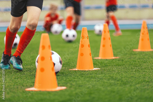 A row of orange soccer training cones. Players running with football balls between practice cones. Soccer training class for children players © matimix