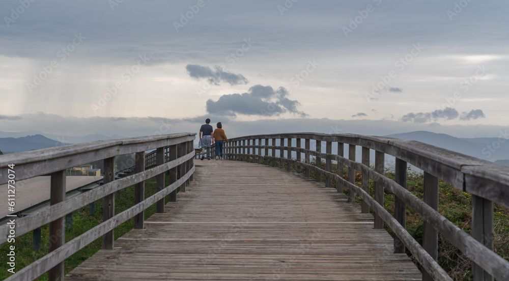 A couple in love man and woman walk along a wooden path on the shores of the Atlantic Ocean on a spring evening at sunset on a cloudy day.