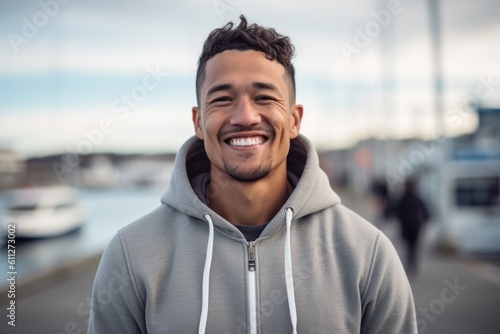 Medium shot portrait photography of a happy boy in his 30s wearing a comfortable hoodie against a picturesque harbor background. With generative AI technology