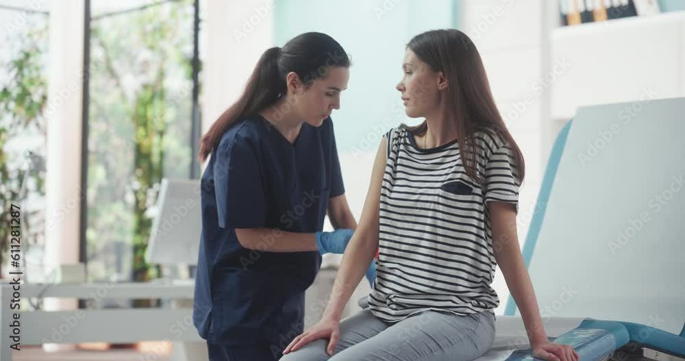 Happy Caucasian Woman Sitting In The Chair In Bright Hospital And Getting Her Hepatitis B Vaccine. Professional Female Nurse Is Performing Injection And Putting A Patch On. Public Healthcare Concept. Happy Caucasian Woman Sitting In The Chair In Bright Hospital And Getting Her Hepatitis B Vaccine. Professional Female Nurse Is Performing Injection And Putting A Patch On. Public Healthcare Concept.