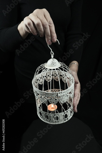 The woman has a cage in her hands. There is a candle in the cage. photo