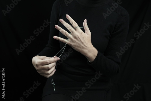 The fingers of a woman's hand are tied with a string. A man's hand holds strings. Dark background.