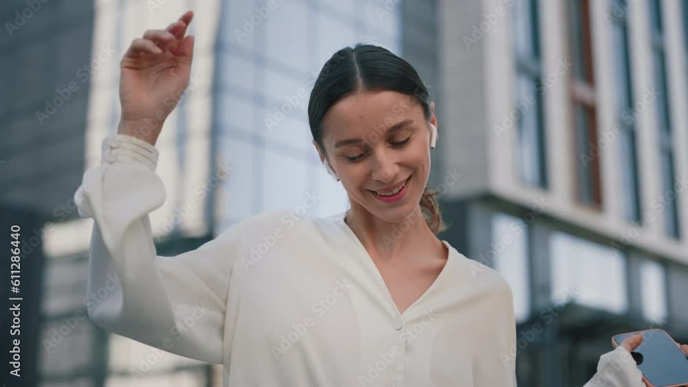 Smiling Caucasian Woman Grooving to Music with Earphones, Smartphone in Hand, Dancing as She Walks. Cute Lady Manager Enjoying her Playlist and Funny Dance Letting the Rhythm Move Her Smiling Caucasian Woman Grooving to Music with Earphones, Smartphone in Hand, Dancing as She Walks. Cute Lady Manager Enjoying her Playlist and Funny Dance Letting the Rhythm Move Her