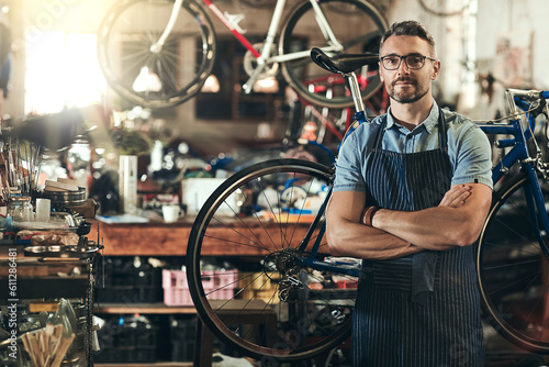 Portrait, serious and repair man in bicycle shop with arms crossed in workshop. Face, bike mechanic and confident male person, professional or mature technician and glasses in store or small business