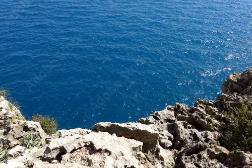 View from high rocky shore to the azure transparent sea water with sunlight reflection in bright sunny day