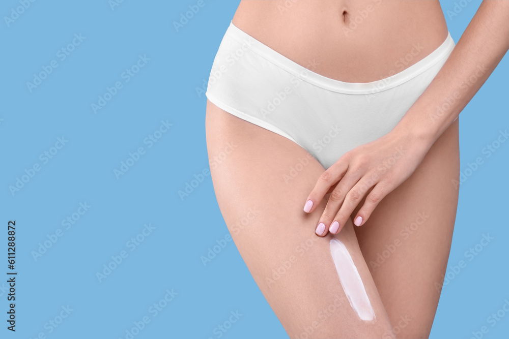 Woman with smear of body cream on her leg against light blue background, closeup. Space for text