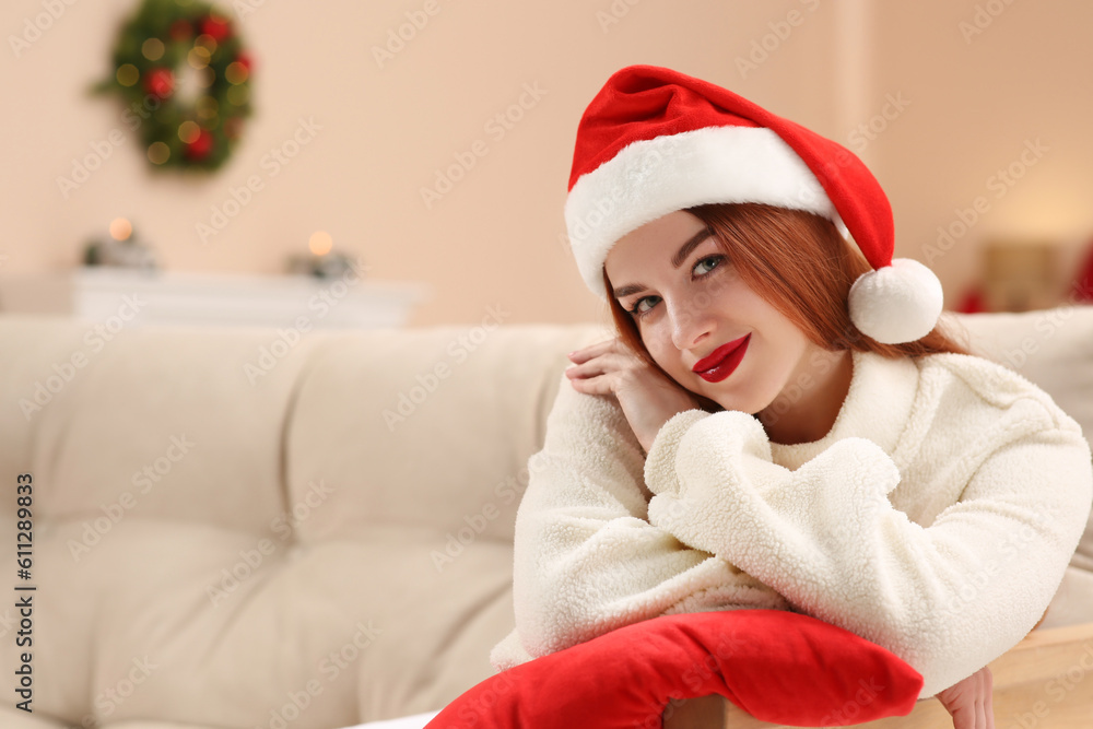 Beautiful young woman in Santa hat on sofa at home, space for text. Celebrating Christmas Beautiful young woman in Santa hat on sofa at home, space for text. Celebrating Christmas