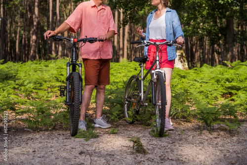 Mature man and his daughter standing with bicycle in the forest road at the summer