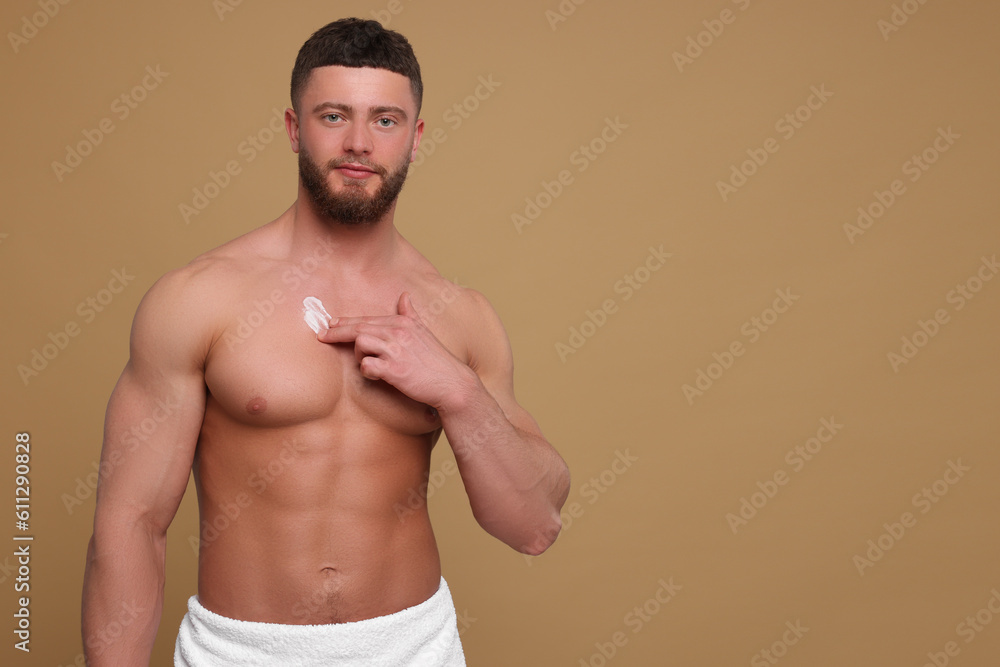 Handsome man applying body cream onto his chest on pale brown background, space for text
