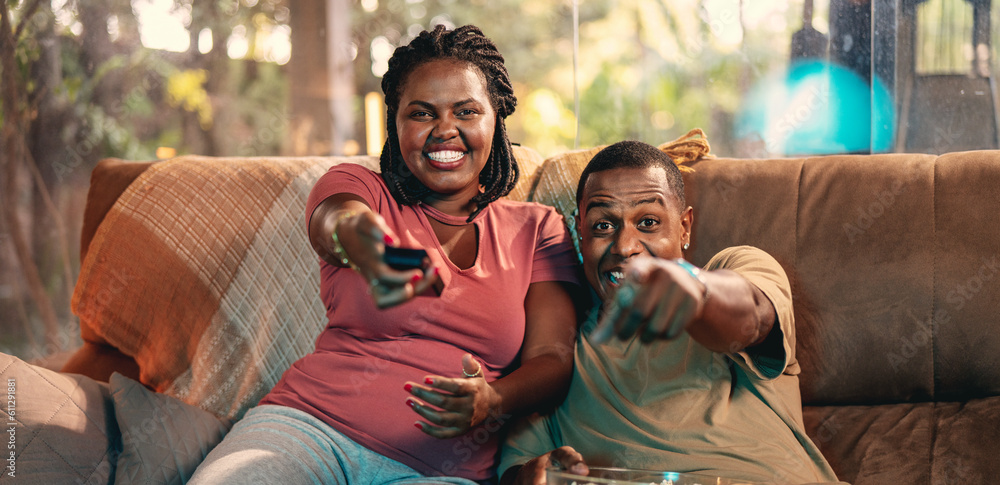 Latin couple eating popcorn sitting on sofa in living room on valentine's day pointing at something on tv