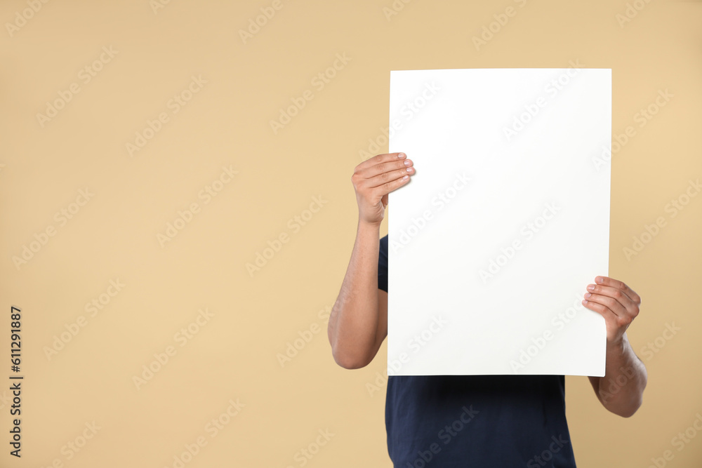 Man holding sheet of paper on beige background, closeup. Mockup for design Man holding sheet of paper on beige background, closeup. Mockup for design