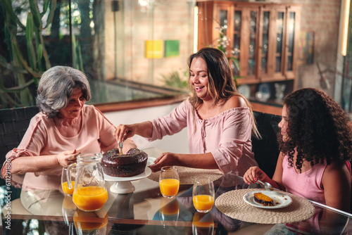 Mulher Brasileira servindo bolo para sua mãe e sua filha na mesa de durante almoço de dia das mães