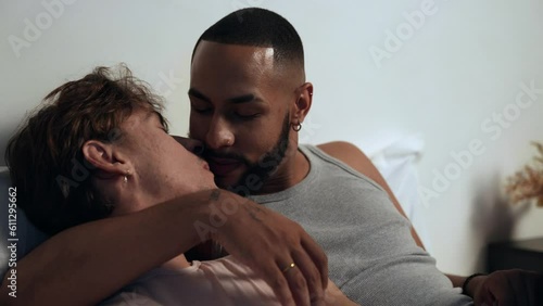 jovem casal gay interracial brasileiro conversando deitados na cama abraçados e se beijando no dia dos namorados photo