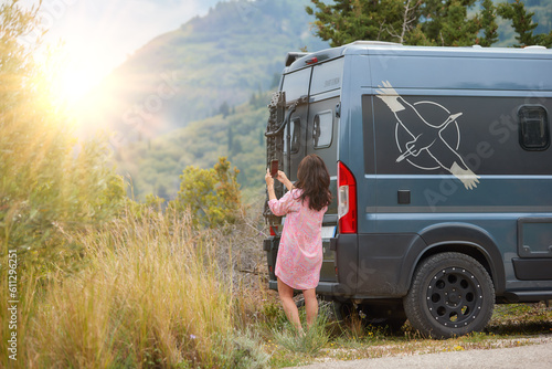 Work and Travel concept, outdoor leisure activity and wanderlust lifestyle - woman next to off road camper van taking pictures by mobil phone of sunset. Spring time, Greece, Lefkada Island.