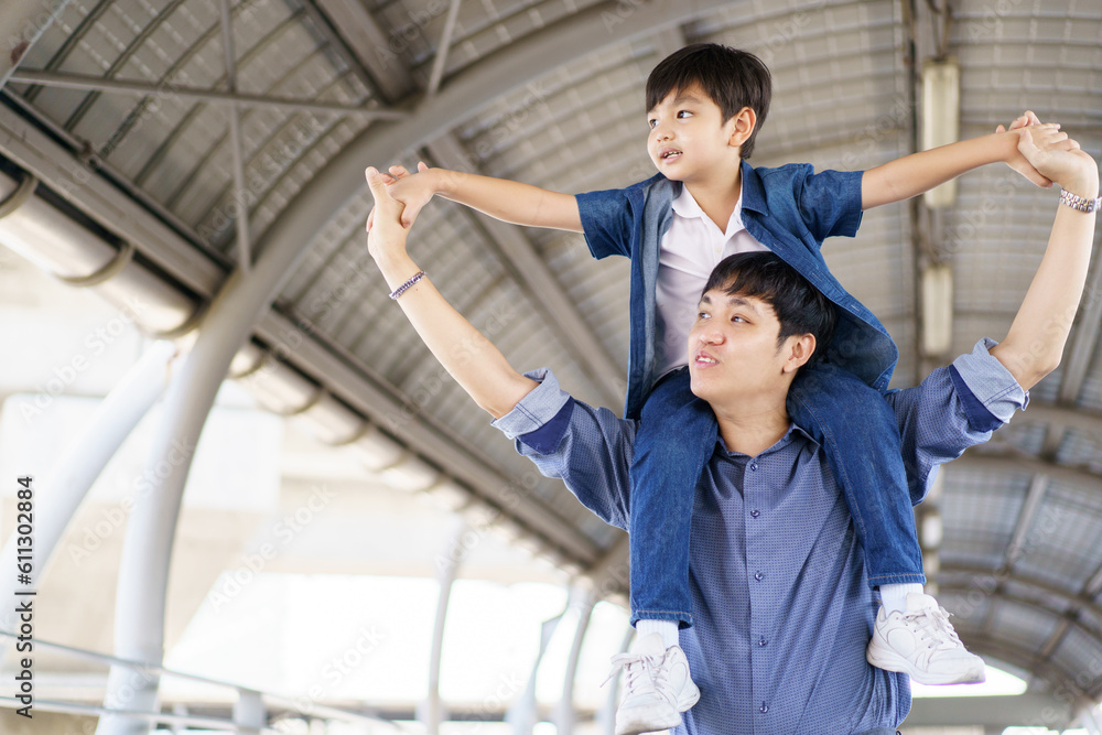 Happy joyful Asian man and lovely son traveling together in the city, dad piggyback son on his back while walking in the city. Man and boy traveling together. Happy joyful Asian man and lovely son traveling together in the city, dad piggyback son on his back while walking in the city. Man and boy traveling together.