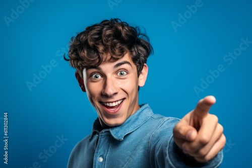 Close-up portrait photography of a happy boy in his 20s pointing at oneself with the index finger against a periwinkle blue background. With generative AI technology