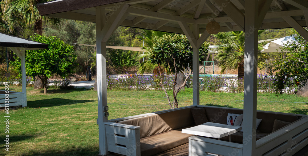 Garden with palm trees, white wooden gazebos and hammocks. Furniture for rest.