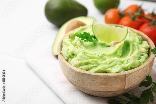 Bowl of delicious guacamole and ingredients on white table, closeup. Space for text