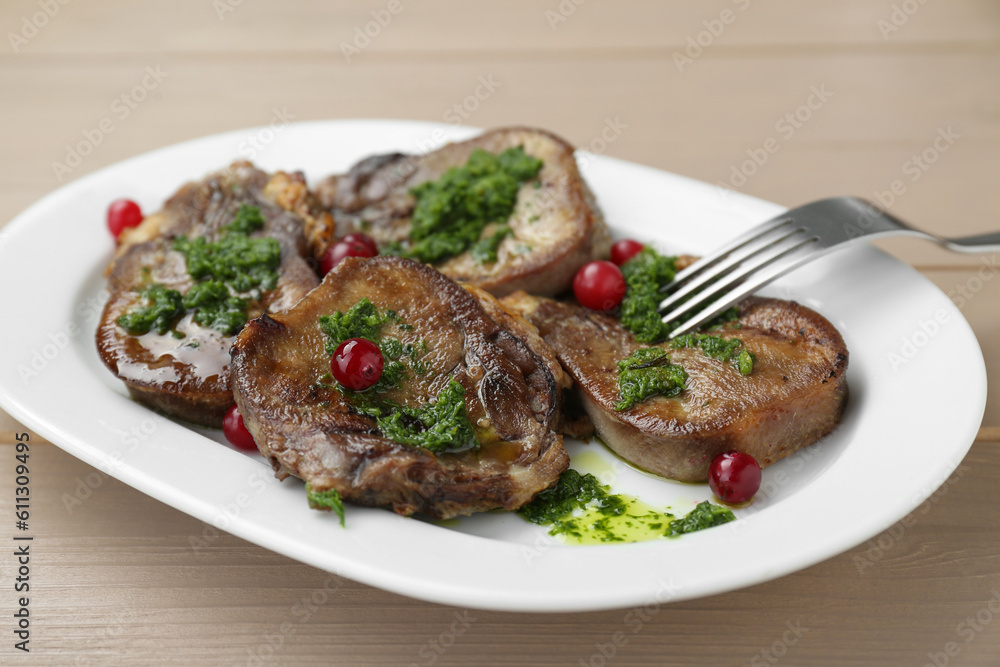 Tasty beef tongue pieces, salsa verde and berries on beige wooden table, closeup