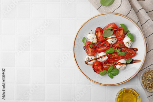 Tasty salad Caprese with mozarella balls, tomatoes, basil and other ingredients on white tiled table, flat lay. Space for text