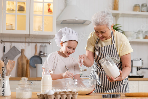 Happy family in kitchen. Grandmother and granddaughter child cook in kitchen together. Grandma teaching kid girl knead dough bake cookies. Household teamwork helping family generations concept