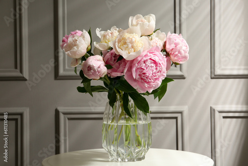 Bouquet of beautiful peonies in glass vase on white table