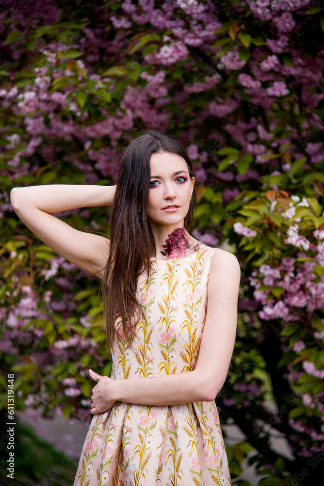 portrait of sensitive beautiful brunette woman with tattoo on her neck in dress in the garden near blossoming sakura flowers portrait of sensitive beautiful brunette woman with tattoo on her neck in dress in the garden near blossoming sakura flowers
