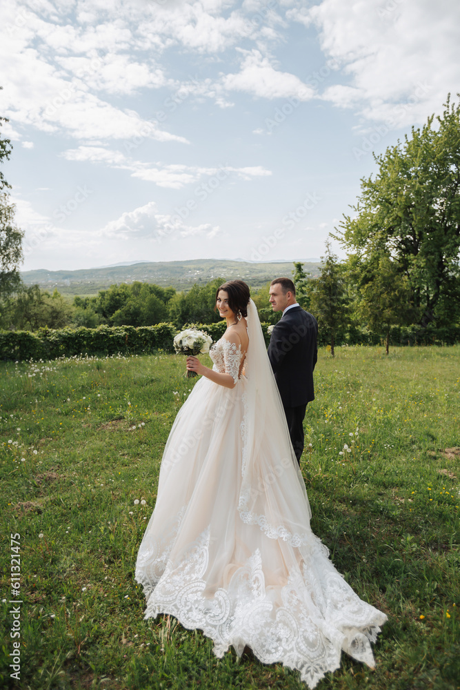Portrait of the bride and groom in nature. A stylish bride and groom in a long lace dress are walking in the garden holding hands. Couple in love