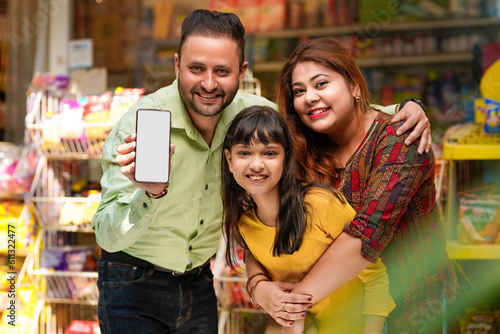 Happy family showing empty smartphone Screen at grocery shop.