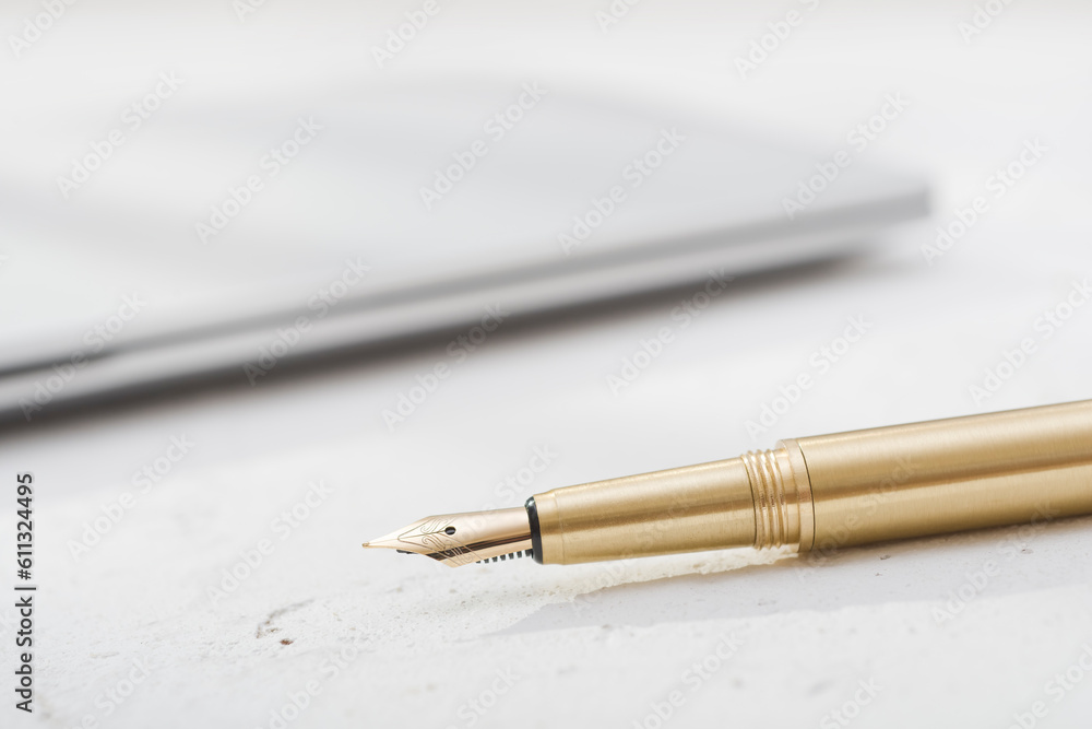 Fototapeta premium Golden fountain pen with blurred notebook on vintage desk surface