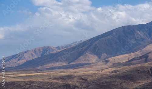 Unusual mountain landscape with bright cloudy skies. Autumn in remote foothills in northern China. Dry grassy and hills. Natural background. Exploration of new places, travel to remote locations.