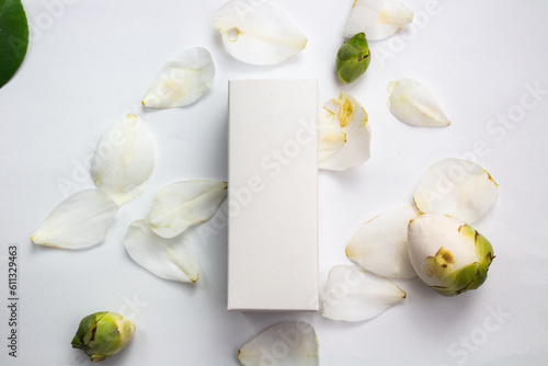 Product photo of a white box of natural cosmetics, on a white background and camellia petals and flowers