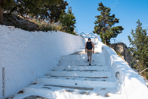 A Man with Knapsack Going Up a Set of White Steps Towards Symi Castle, Greece on a Sunny Day
