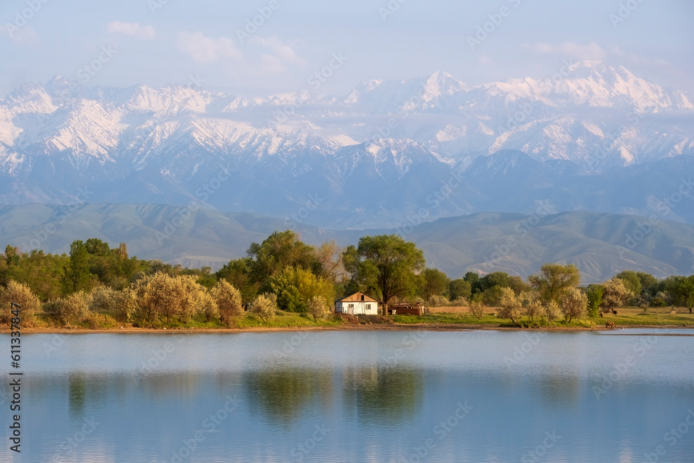 Small white house on lake near high snowy mountains in summer