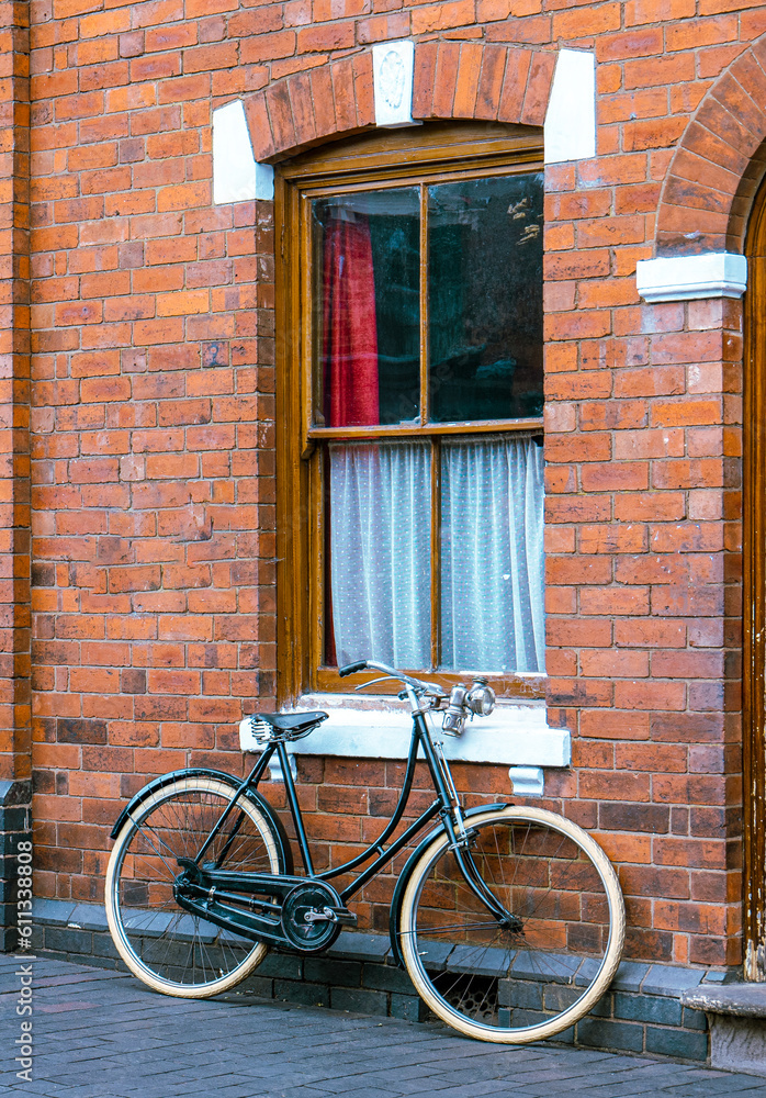 Old ladies bicycle leans against redbrick house wall with net sash windows 