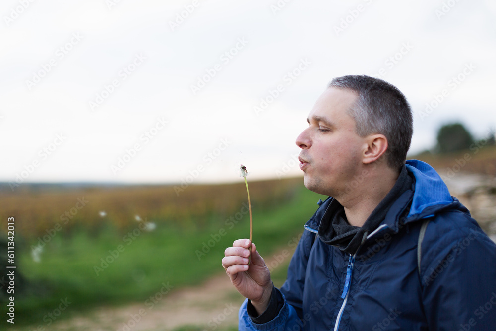 A man blowing a dandelion with the vineyards at the background A man blowing a dandelion with the vineyards at the background