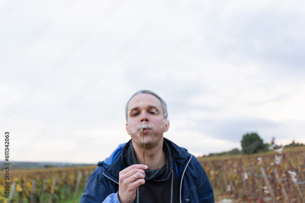 A man blowing a dandelion with the vineyards at the background A man blowing a dandelion with the vineyards at the background