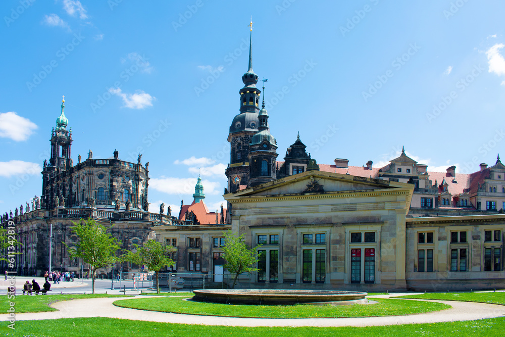 Square with old buildings with towers and spires and decorative elements on the facades. Historical architecture. Old town. Sunny day with blue sky and green lawns. Dresden, Germany, May 2023.