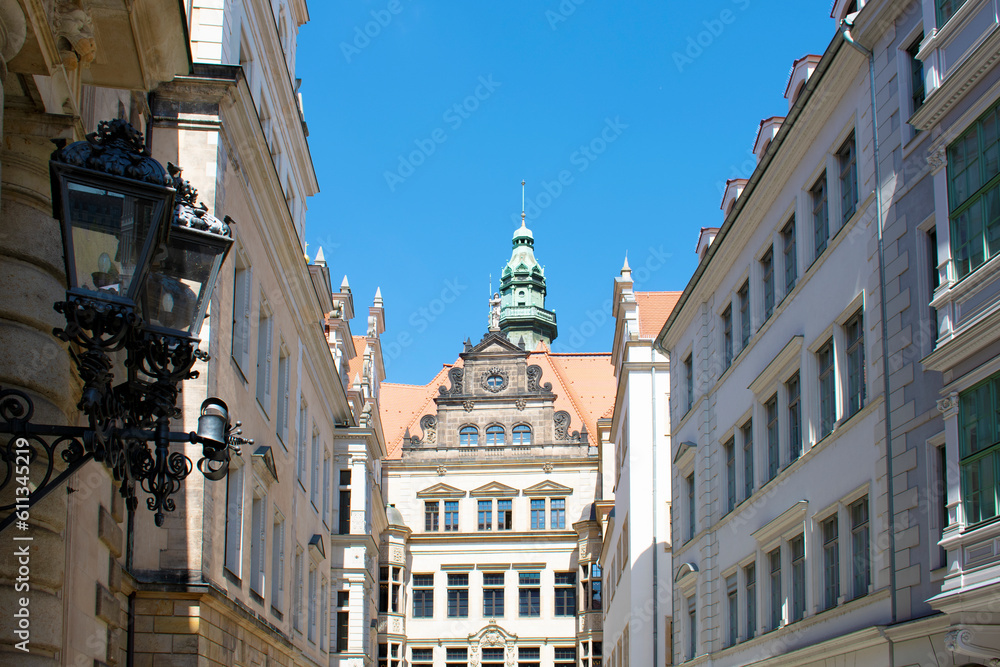 View of an old building with tower and red roof, line of facades of buildings and street metal forged lantern. Old architecture. Sunny day with blue sky. Dresden, Germany, May 2023.