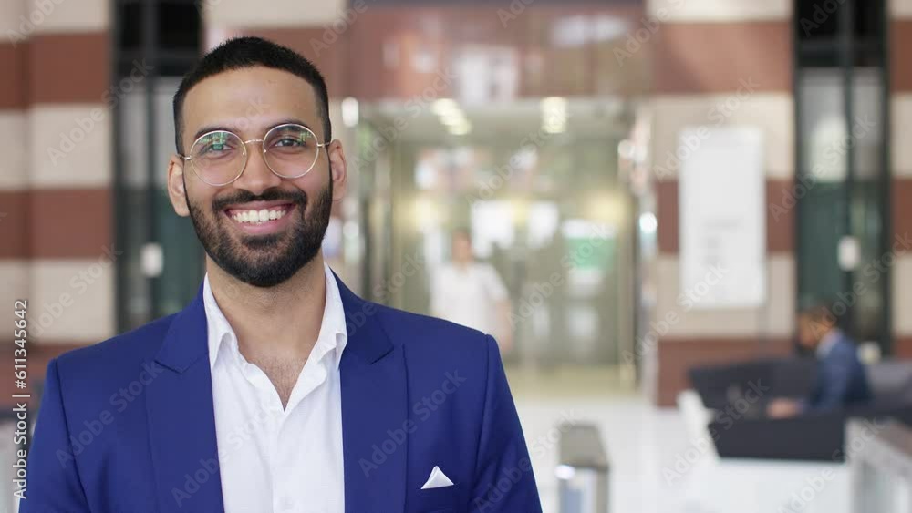Camera tilts up to reveal portrait of cheerful Indian professional looking to camera and smiling in a building lobby Camera tilts up to reveal portrait of cheerful Indian professional looking to camera and smiling in a building lobby