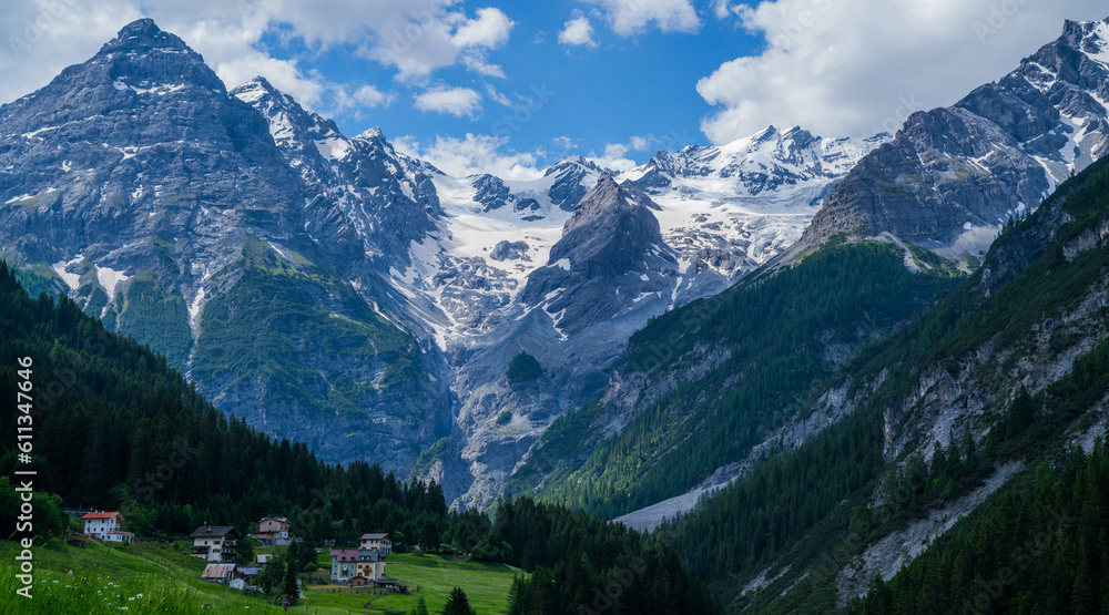 Landscape of the Alps. Snow-capped mountain peaks and beautiful meadows. Freedom, tourism, travel. Peaks on a background of white clouds and blue sky. Green hills and dense forests on the slopes.