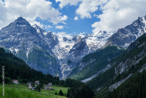 Landscape of the Alps. Snow-capped mountain peaks and beautiful meadows. Freedom, tourism, travel. Peaks on a background of white clouds and blue sky. Green hills and dense forests on the slopes. © eskstock