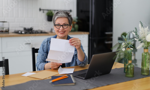 Photography A woman joyfully reads a letter or invitation while sitting at table with a laptop