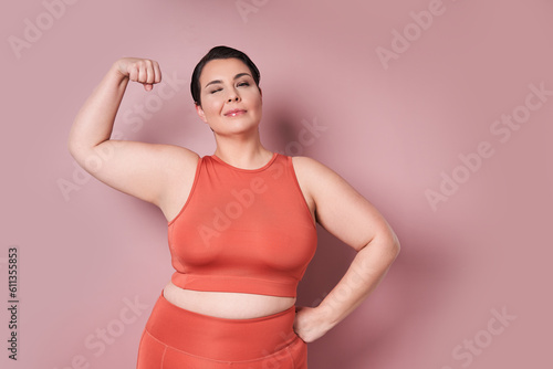 Cheerful large woman showing biceps on pink background