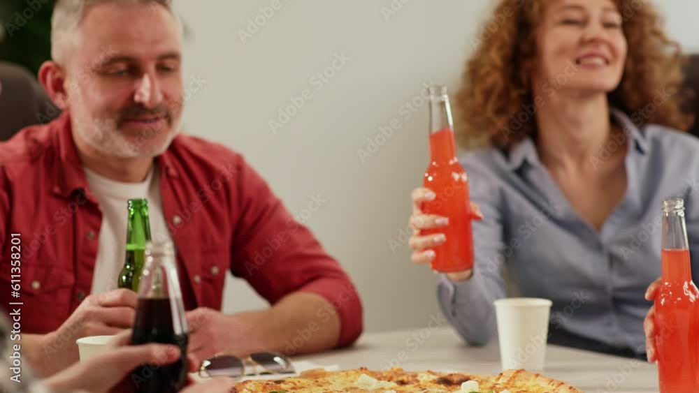 A team of workers sits at a table and clinks glasses with glass bottles. Office workers eat pizza and drink soda during their lunch break. A team of workers sits at a table and clinks glasses with glass bottles. Office workers eat pizza and drink soda during their lunch break.