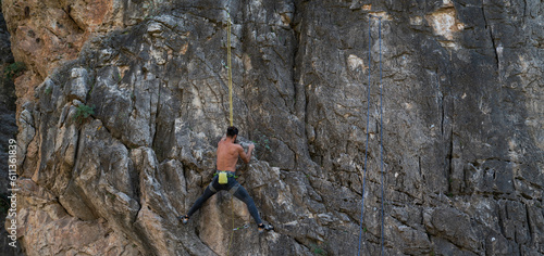 View from behind of a young male rock climber. Powerful male rock climber climbing on a vertical rock face. A man trains strength and endurance, overcoming the fear of heights, training in nature.