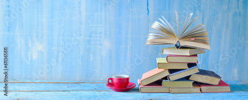 Open book, hardback books and cup of coffee on blue background.Literature, education,reading and relaxing concept. Panoramic with large copy space