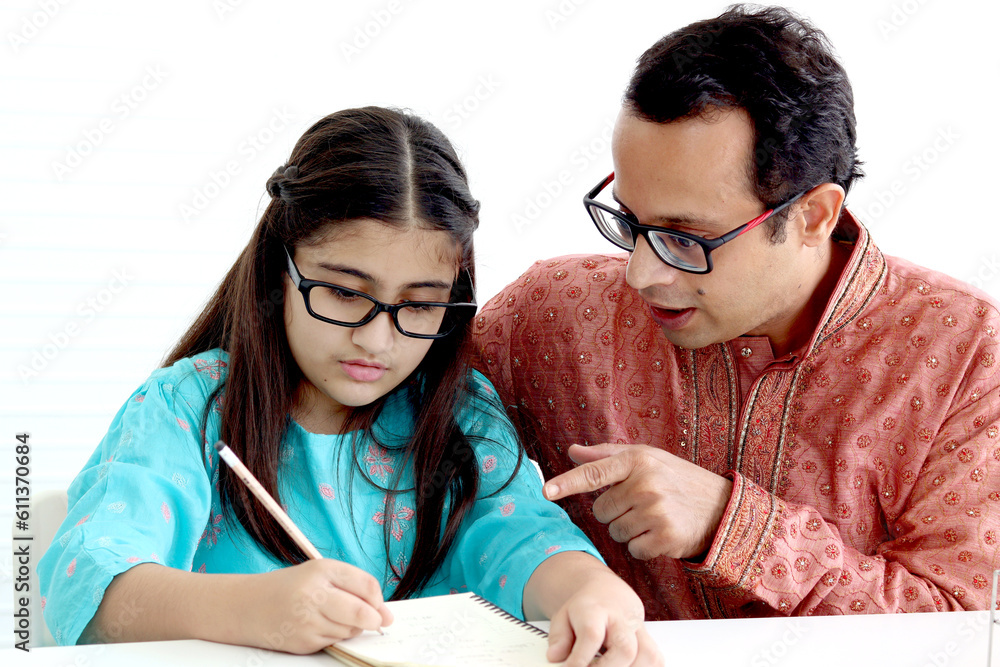 Cute Indian school student girl in traditional dress and glasses do homework with father, father teaching daughter kid at home, parent become teacher tutor involvement in childhood education in family Cute Indian school student girl in traditional dress and glasses do homework with father, father teaching daughter kid at home, parent become teacher tutor involvement in childhood education in family